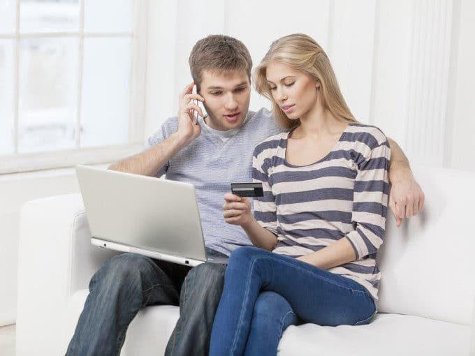 photo: couple seated on couch with telephone, computer, and credit card